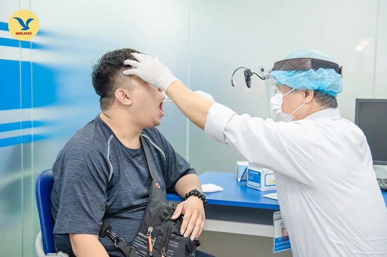Bác sĩ đang tiến hành thăm khám cổ họng cho bệnh nhân để chẩn đoán nguyên nhân đau họng